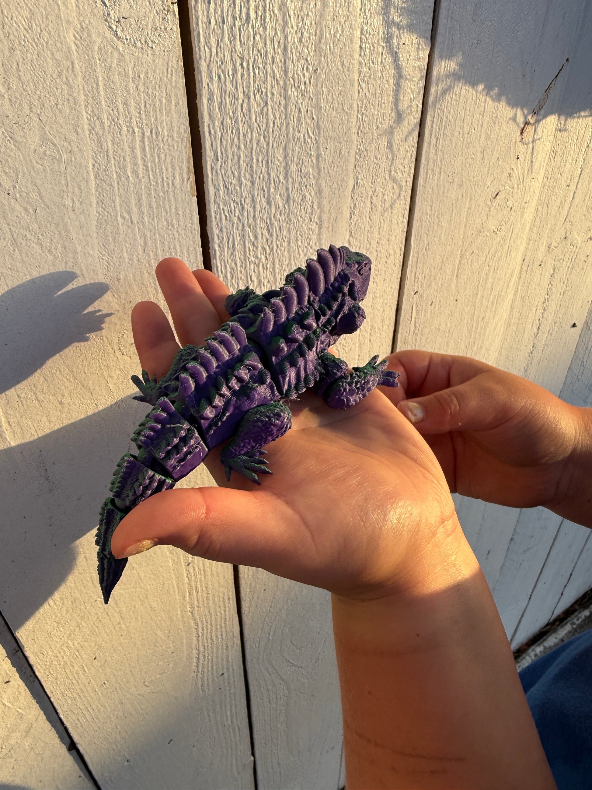 Purple and green articulated chameleon 3D print held in hands